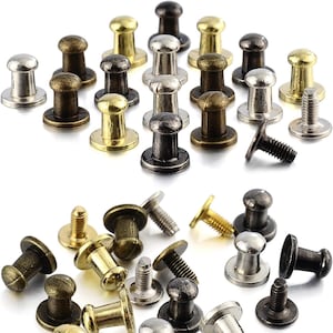 Może przedstawiać: Zbiór metalowych gwoździ do mebli w różnych wykończeniach, w tym złote, srebrne i czarne. Gwoździe mają okrągłą główkę z wypukłym środkiem i gwintowany trzpień.