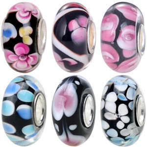 May include: Six glass beads with different floral and abstract patterns. The beads are black with white, pink, and blue accents. The beads have silver metal accents.