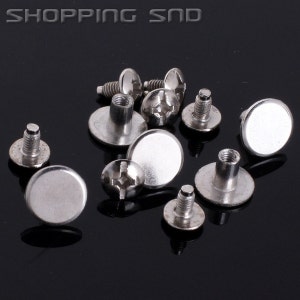 May include: A close-up of silver metal screw-on studs with a flat top. The studs are scattered on a black surface.