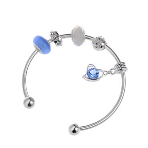 Op de afbeelding: Een zilveren armband met een blauwe en witte bedel, een hartbedel met een blauwe kristal en een zilveren kraal met een witte kristal.