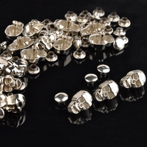 May include: Silver skull-shaped metal rivets, some with a post for attaching to fabric. There are also several plain silver round rivets.