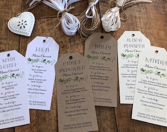 May include: Ten brown and white paper tags with green foliage designs and handwritten text. The tags are labeled with names and the words "Menu Choices". The text includes menu items such as "Spicy Tomato and Basil Soup", "Salmon Teriyaki with Asian Noodles", "Beef Wellington with Dauphinoise Potatoes", "Crispy Aromatic Duck Salad with Plum Sauce and Pomegranate", and "Chicken in White Wine and Cream Sauce with Herbed New Potatoes".