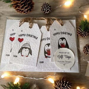 May include: A pack of 10 white gift tags with a penguin design and the text "Happy Christmas". The tags are tied with twine and have a circle sticker that says "Pack of 10 Gift Tags Aarlotte Designs".
