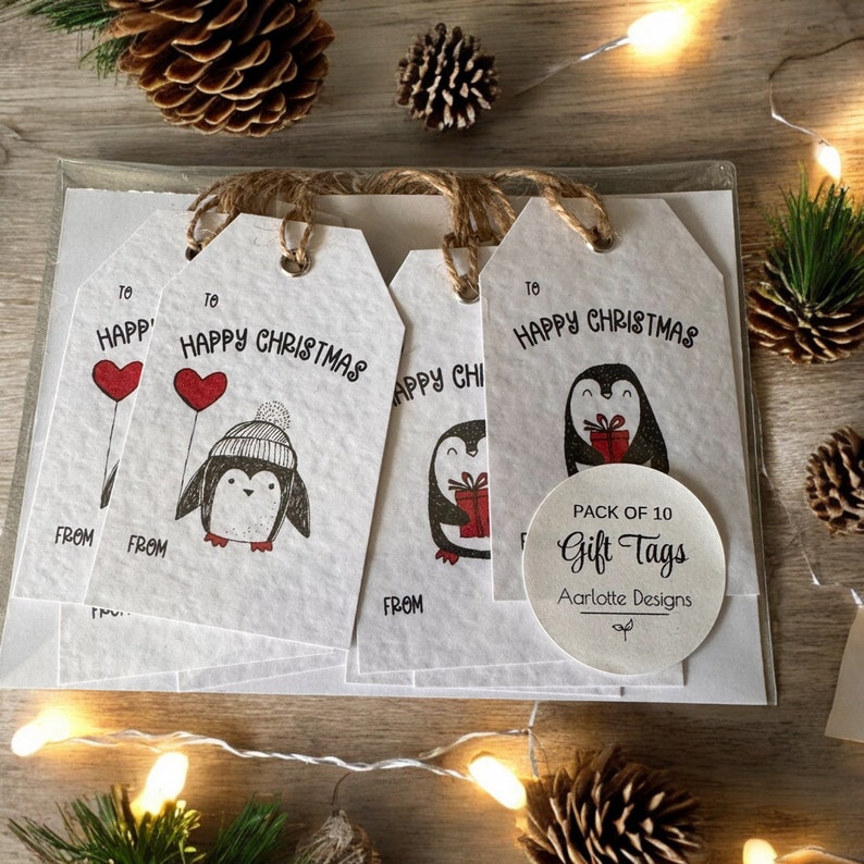 May include: A pack of 10 white gift tags with a penguin design and the text "Happy Christmas". The tags are tied with twine and have a circle sticker that says "Pack of 10 Gift Tags Aarlotte Designs".