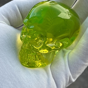Puede incluir: Una escultura de calavera de vidrio verde brillante. La calavera está detallada con una representación realista de los dientes y las cuencas de los ojos.