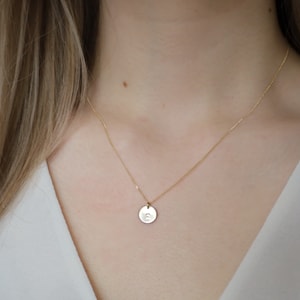 May include: A gold chain necklace with a small, round pendant featuring a single letter.