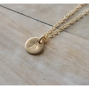 May include: A gold chain necklace with a small round pendant featuring the letter "D" engraved on it.