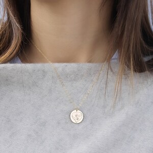 May include: Gold necklace with a round pendant featuring an engraved heart with two hands inside.