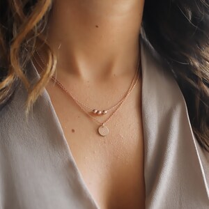 May include: A layered rose gold necklace with a small round pendant. The pendant has a single initial engraved on it.