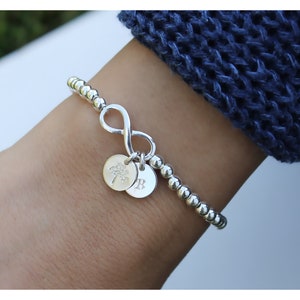 May include: A silver beaded bracelet with an infinity charm and two small charms, one with a tree design and the other with the letter "B".