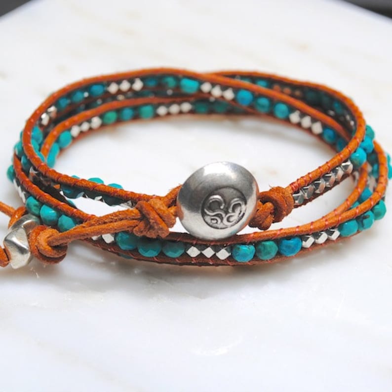 May include: Wrap bracelet featuring turquoise beads, silver accents, and a brown leather strap. The bracelet has a silver button clasp and is designed to wrap multiple times around the wrist. A stylish accessory for everyday wear.