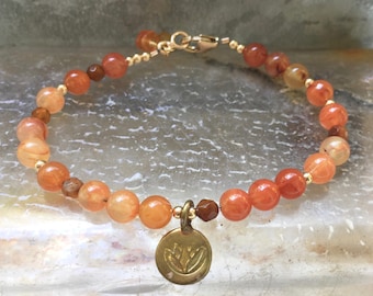 May include: A gold bracelet with orange and brown beads and a gold charm with a flower design.