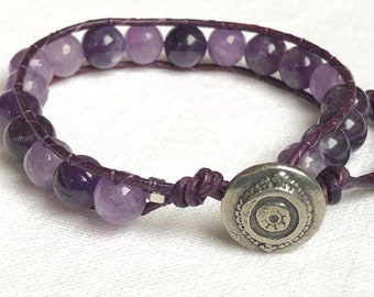 May include: A purple amethyst gemstone bracelet with a silver clasp. The bracelet is made with leather cord and features multiple amethyst beads.