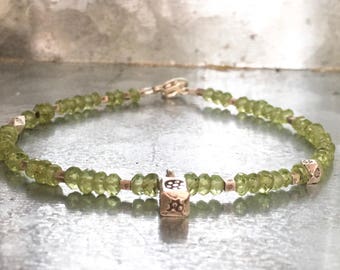 May include: A delicate bracelet featuring small, light green peridot beads strung together. The bracelet includes small, square, silver-toned accent beads and a silver clasp. The focal point is a small, gold-toned charm.