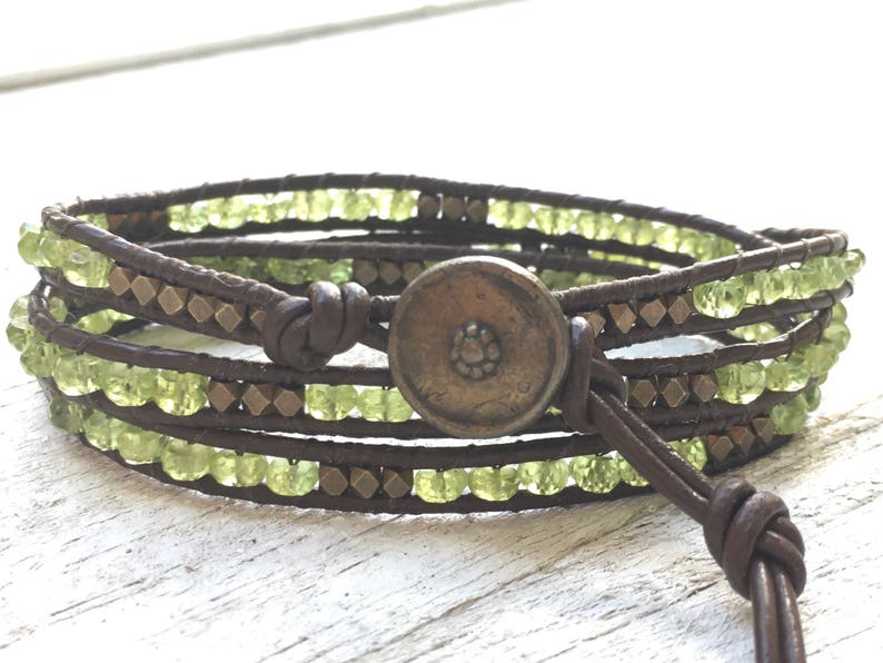 Op de afbeelding: Een bruin leren wikkelarmband met groene edelsteen kralen en een messing knoopsluiting.