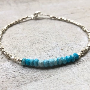 May include: A silver chain bracelet with a gradient of turquoise blue gemstone beads.