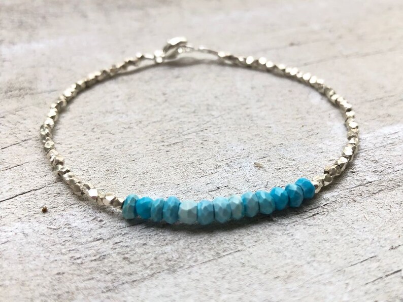 May include: A silver chain bracelet with a gradient of turquoise blue gemstone beads.