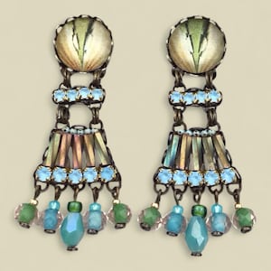 Puede incluir: Un par de pendientes ornamentados con una parte superior circular con un diseño verde y beige. Los pendientes tienen detalles en azul claro e iridiscentes, con cuentas colgantes en tonos verdes, azules y rosas. El metal tiene un acabado bronce.