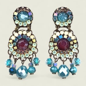 Puede incluir: Un par de pendientes ornamentados con una estética vintage. Cada pendiente presenta una gema grande, facetada de color turquesa en la parte inferior, con gemas y cuentas turquesas y azules más pequeñas. Los pendientes tienen una gema central granate.