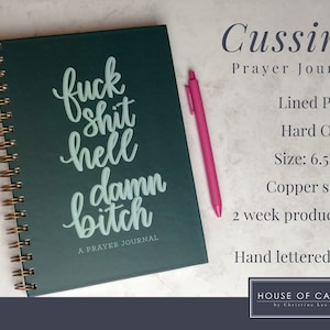 May include: A dark green prayer journal with a copper spiral binding. The cover features the text "fuck shit hell damn bitch" in a light green color. The journal is 6.5 inches by 9 inches and has lined pages. The text "A Prayer Journal" is printed below the main text.