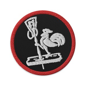 Può includere: Una toppa ricamata rossa e nera con un gallo bianco in piedi su una piattaforma con un microfono. Il gallo è rivolto verso il lato sinistro della toppa.