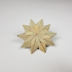 May include: A woven star ornament made from natural materials, with a light brown color and a slightly textured surface.