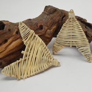 May include: Two woven, light brown, triangular ornaments made of thin strips of natural material. The ornaments are sitting on a piece of weathered driftwood.
