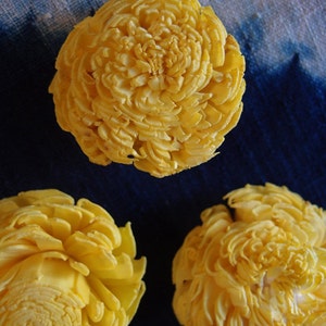 Puede incluir: Tres objetos decorativos de madera tallada con forma de flor, de color amarillo. Los objetos están dispuestos sobre un fondo azul.