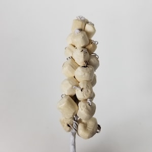 Puede incluir: Un grupo de pequeños adornos redondos de cerámica blanca están enhebrados en un cordón blanco. Los adornos están dispuestos en una línea vertical, que se asemeja a un árbol pequeño.