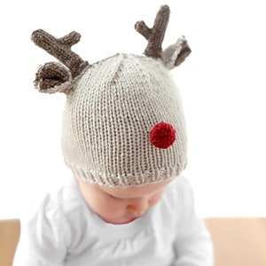 Könnte beinhalten: Eine gestrickte Rentiermütze mit braunen Geweih, einer roten Bommelnase und einem beigefarbenen Strick. Die Mütze wird von einem Baby getragen.