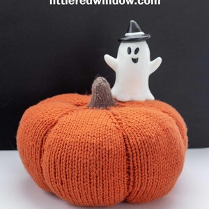 May include: A knitted orange pumpkin with a brown stem and a white ghost wearing a black hat on top. The text "Big Squishy Pumpkin Knitting Pattern" and "littleredwindow.com" is visible on a black background.