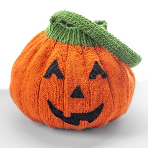 May include: An orange knitted Jack-o'-Lantern trick-or-treat bag with a green handle. The bag has a carved face with black eyes and a mouth. The text "Jack-o'-Lantern Trick-or-Treat Bag Knitting Pattern" is at the top of the image.