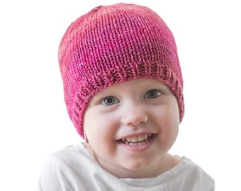 Könnte beinhalten: Ein kleines Kind trägt eine gestrickte rosa Mütze. Die Mütze ist ein einfaches, leichtes Strickmuster. Der Text "Basic Easy Hat Knitting Pattern" und "littleredwindow.com" ist über dem Kopf des Kindes sichtbar.