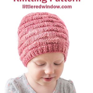 May include: A pink knitted hat with a basketweave pattern. The hat is being worn by a young child. The text "Basketweave Hat Knitting Pattern" and "littleredwindow.com" is visible at the top of the image.