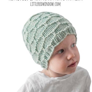 May include: A child wearing a light green knitted hat with a honeycomb pattern. The hat is made with a simple stitch and has a slouchy fit. The hat is titled "Honeycomb Hat Knitting Pattern" with the website "littleredwindow.com" below the title.