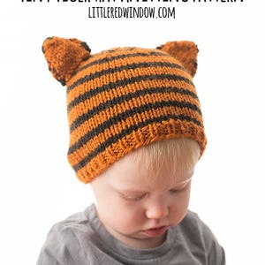 May include: A child wearing a striped orange and brown knitted hat with tiger ears. The hat is made with a knit stitch and has a simple design.