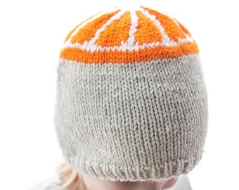 Puede incluir: Un niño lleva una gorra de punto gris con un diseño de cítricos naranja y blanco. La gorra tiene una textura acanalada y un borde doblado. El texto "Citrus Hat Knitting Pattern" y "littleredwindow.com" se muestra sobre la gorra.