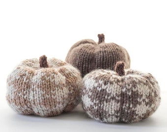 Op de afbeelding: Drie gebreide pompoenen in een bruin en wit buffalo plaid patroon. De pompoenen liggen op een wit oppervlak. De tekst "Buffalo Plaid Pumpkin Knitting Pattern littleredwindow.com" staat boven de pompoenen.