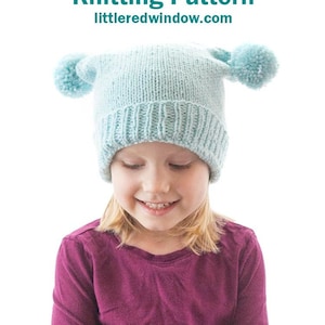 May include: A light blue knitted hat with two fluffy pom-poms on top. The hat is worn by a child with blonde hair and a purple shirt. The text "Double Pom Pom Hat Knitting Pattern littleredwindow.com" is displayed above the hat.