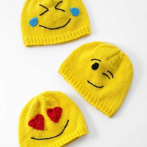 Puede incluir: Tres gorros de punto amarillos con diferentes caras de emoji. Los gorros presentan una cara guiñando un ojo, una cara llorando y una cara con corazones por ojos. Los gorros están sobre un fondo blanco. Emoji Hats Knitting Pattern littleredwindow.com