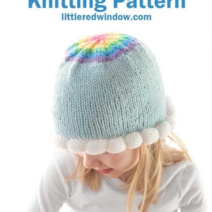 May include: A light blue knitted hat with a white pom-pom trim and a rainbow knit detail on the crown. The hat is worn by a child with blonde hair. The text "Cloud Brim Hat Knitting Pattern" and "littleredwindow.com" is displayed above the hat.
