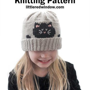 Könnte beinhalten: Ein Kind trägt eine graue Strickmütze mit einem schwarzen Katzenkopf-Design. Die Mütze hat rosa Wangen und Schnurrhaare. Der Text "Peekaboo Black Cat Hat Knitting Pattern littleredwindow.com" befindet sich über der Mütze.