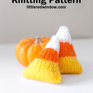May include: Two knitted candy corn hand warmers, one yellow, orange, and white, and the other orange, white, and yellow, with a small orange pumpkin in the background.