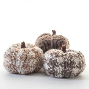 May include: Three knitted pumpkins in brown and white buffalo plaid pattern. The pumpkins are on a white surface. The text "Buffalo Plaid Pumpkin Knitting Pattern littleredwindow.com" is above the pumpkins.