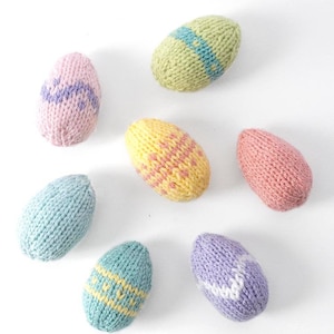 Seven knit Easter Eggs in pastel colors of pink lavender light blue yellow and light green with different stripe patterns arranged in a circle on a white background