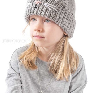May include: A gray knitted beanie with a cat face design. The cat face has black eyes, a pink nose, and white whiskers.
