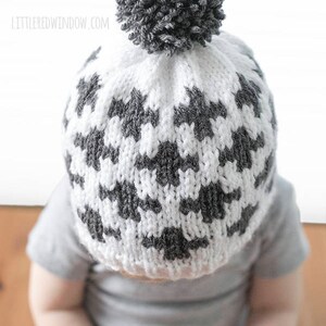 Puede incluir: Un gorro de punto blanco y gris con un pomp&oacute;n gris en la parte superior. El gorro tiene un patr&oacute;n geom&eacute;trico.