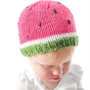 baby wearing a fun knit hat that looks like a watermelon slice complete with seeds looking down to the right