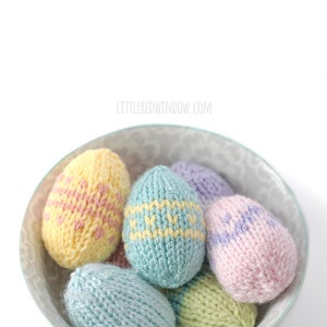 view from above of pastel colored knit easter eggs with various easter egg stripe patterns piled in a gray bown on a white table top