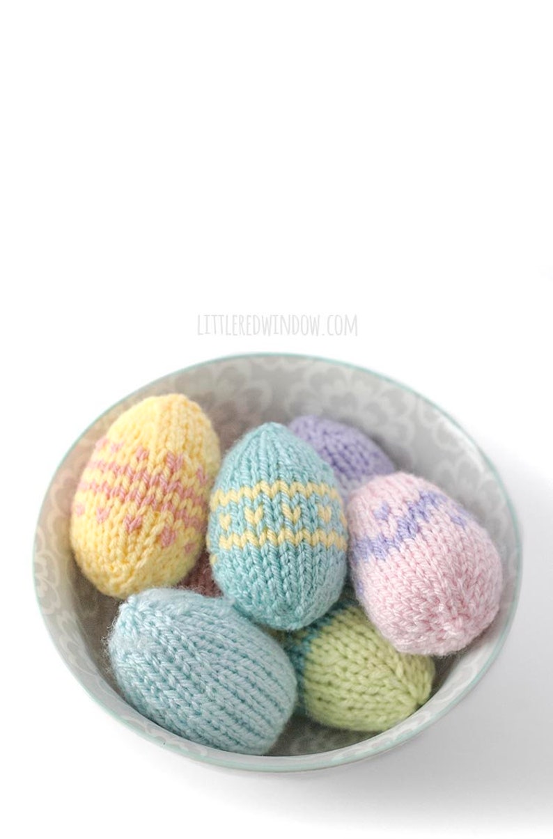 view from above of pastel colored knit easter eggs with various easter egg stripe patterns piled in a gray bown on a white table top